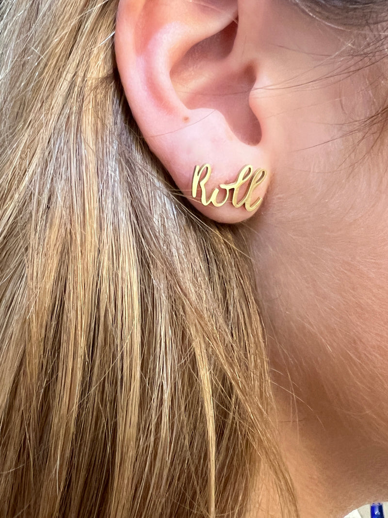 Gold 'Roll' earrings worn by a person with blonde hair.